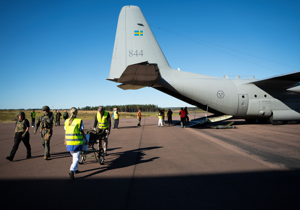 ett flygplan står på en landningsbana och sjukvårdare och militär går på marken