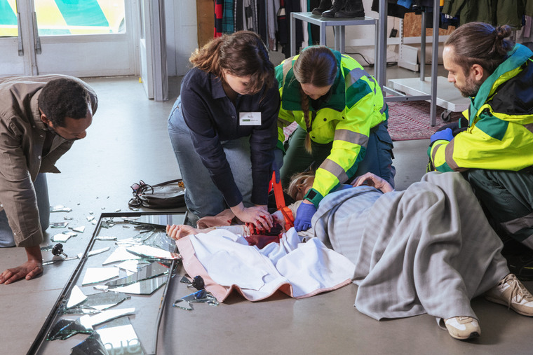 Kvinna och ambulanspersonal stoppar en blödning på en person.